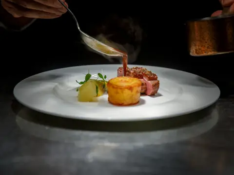 Mood photo (not the venue): Chef finishing a plated dish with sauce
