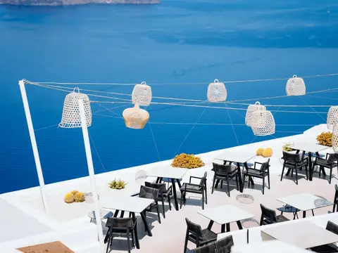 Mood photo (not the venue): White terrace restaurant with lanterns above a blue sea