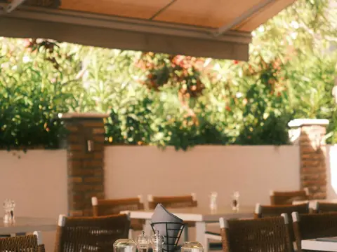 Mood photo (not the venue): Sunlit restaurant patio with woven chairs